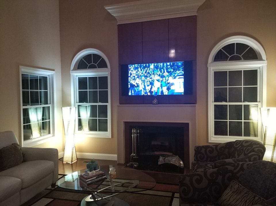 Cozy living room with lit lamps, arched windows, fireplace, and TV mounted above the mantel by Audio Video Concepts