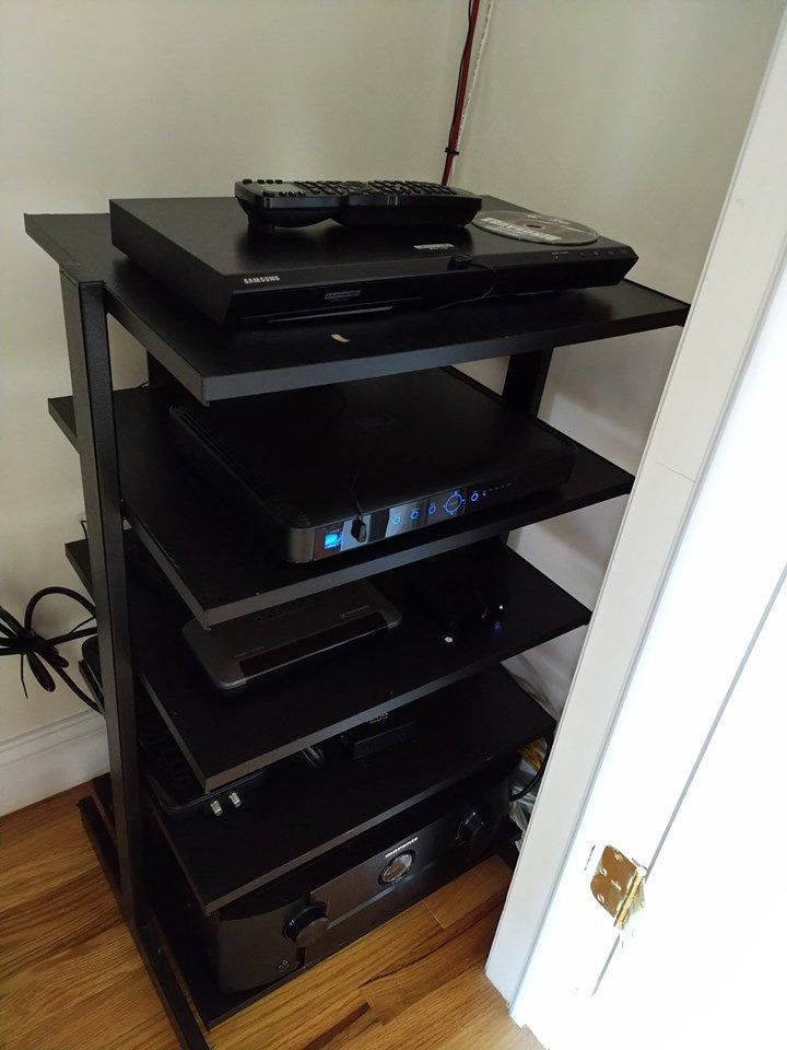 Black media cabinet with stacked electronics and cables in a corner of a room by Audio Video Concepts
