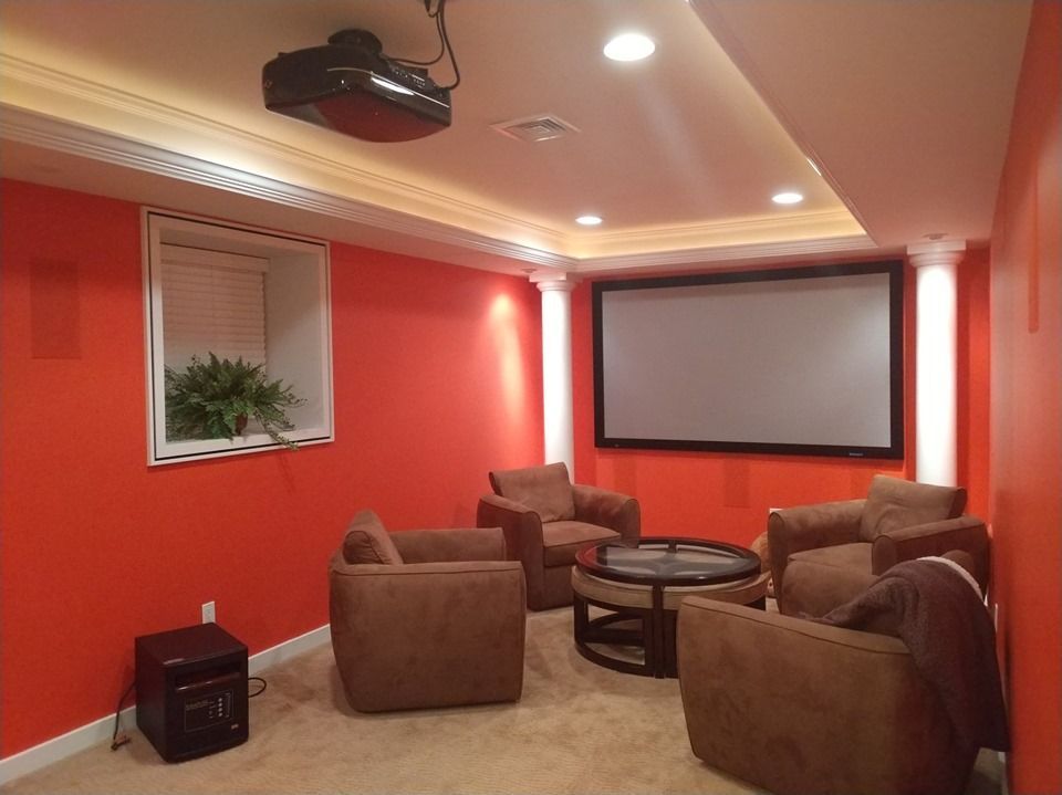 Cozy home theater with red walls, projector screen, and brown armchairs around a round table by Audio Video Concepts
