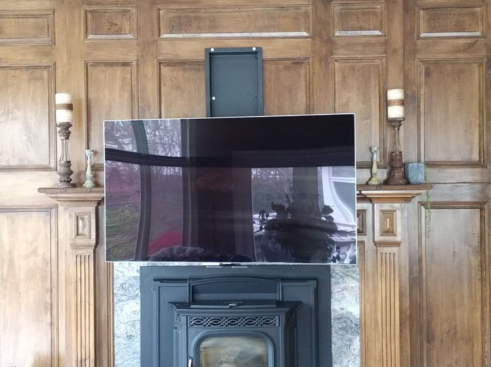 Flat-screen TV mounted above a fireplace in a wood-paneled room by Audio Video Concepts