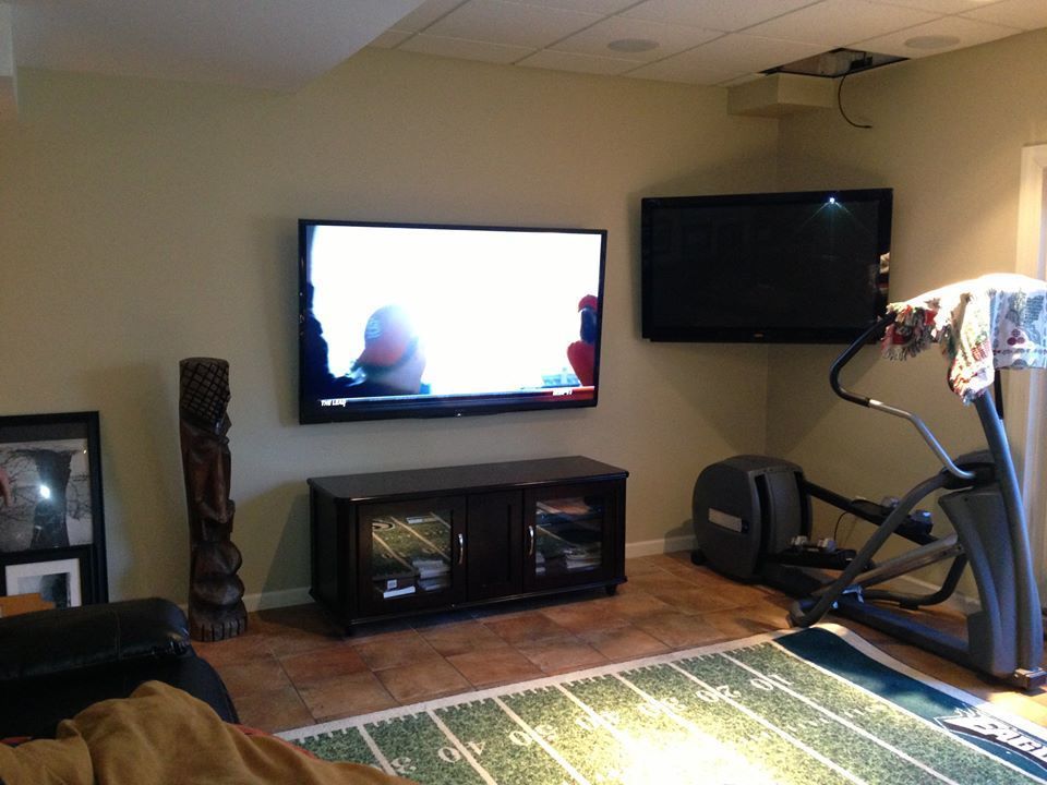 Living room with two wall-mounted TVs, fireplace, exercise bike, and rug on hardwood floor by Audio Video Concepts
