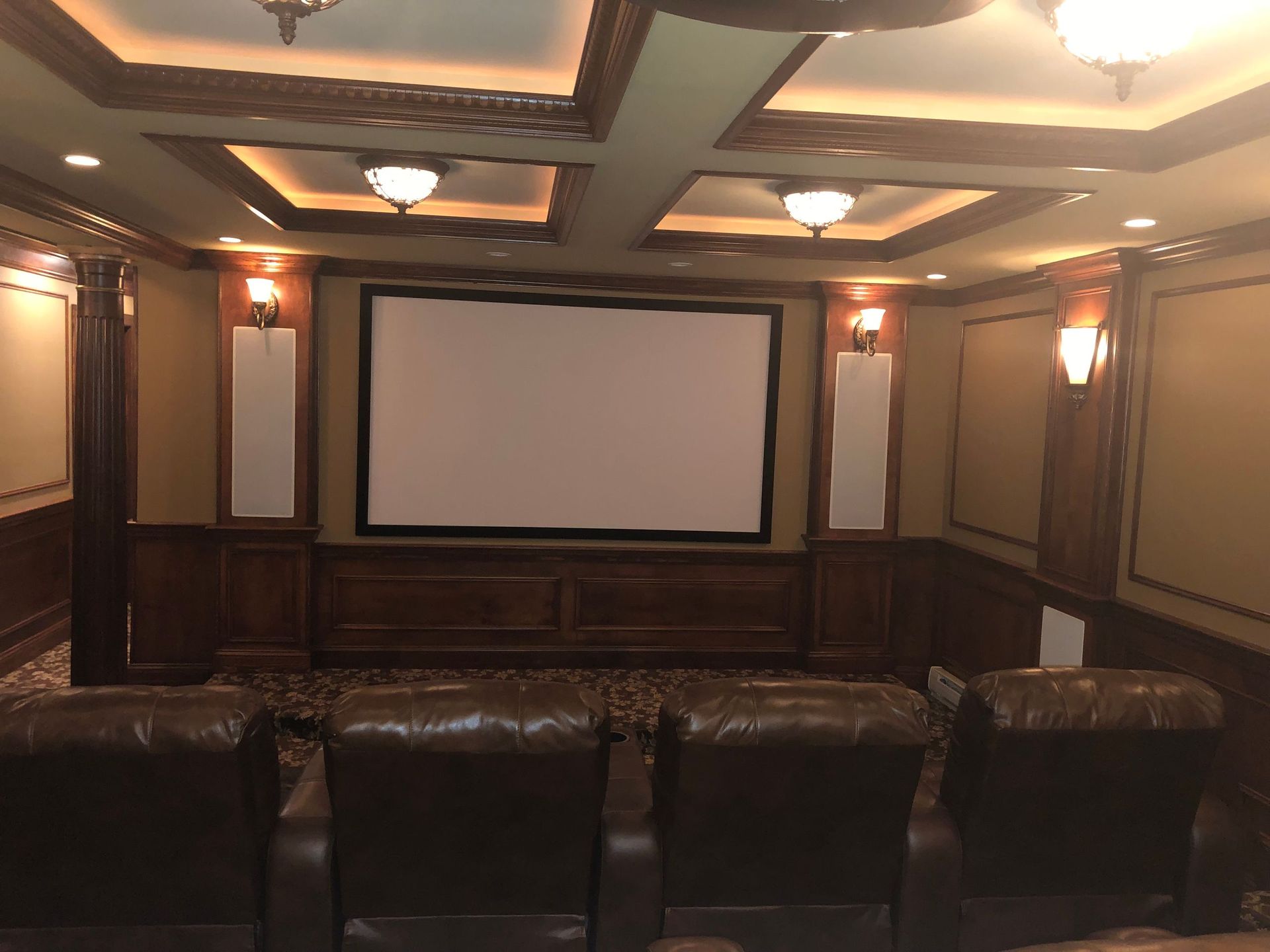 Home theater room with leather recliners facing a large projection screen and wood-paneled walls by Audio Video Concepts