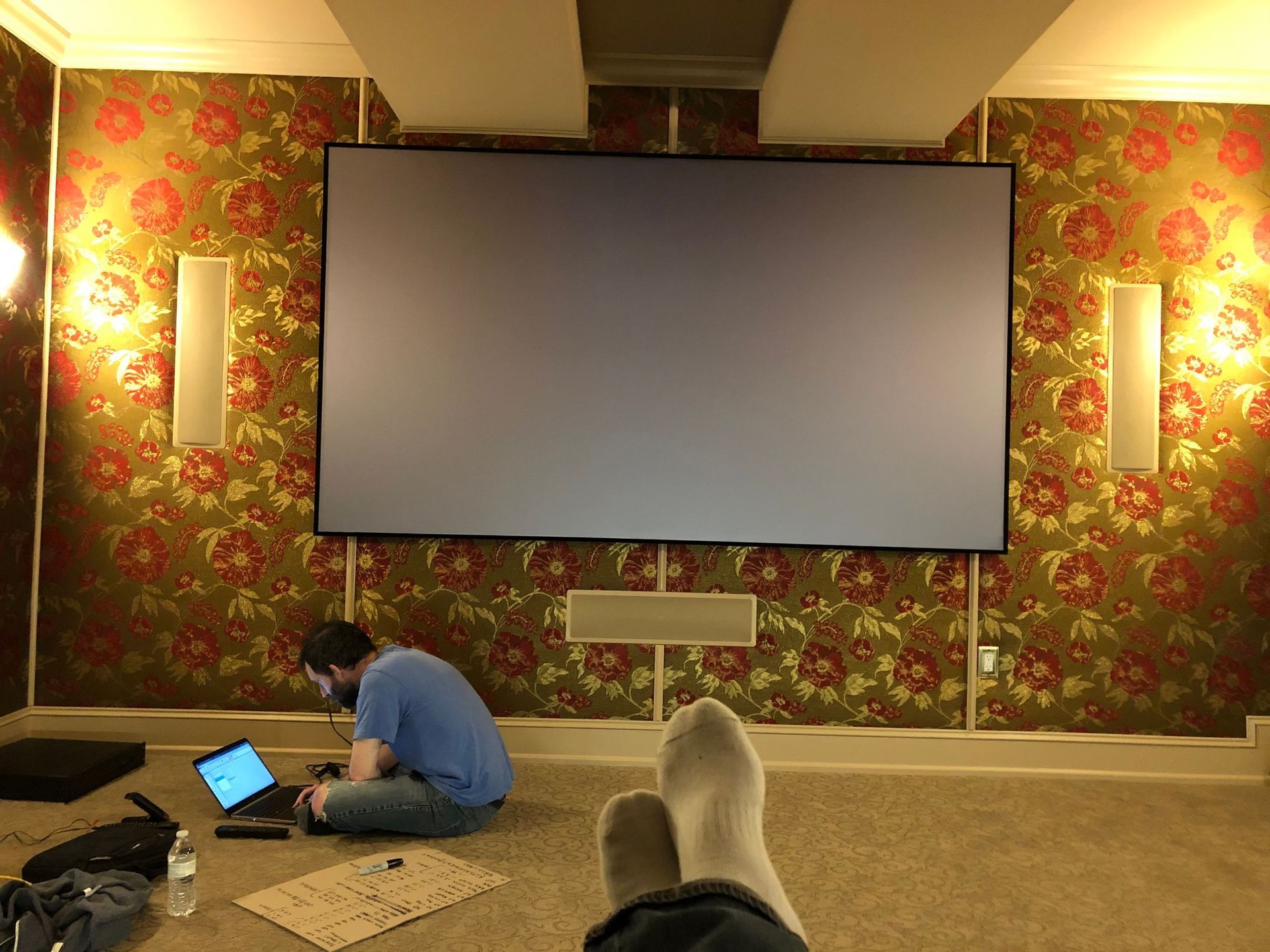 A person sits on the floor with a laptop facing a large projection screen in a patterned room by Audio Video Concepts