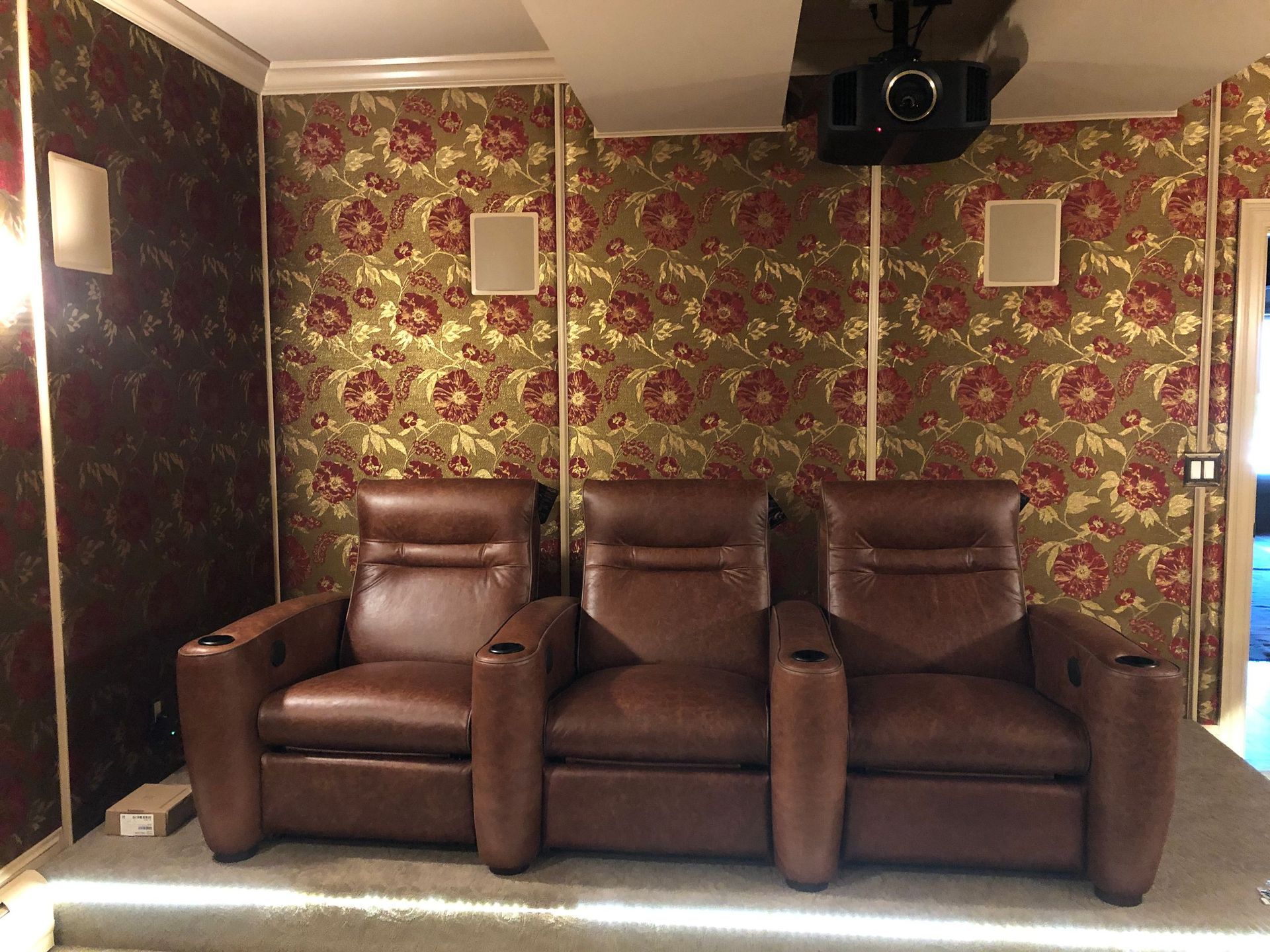 Three brown recliner chairs in a floral wallpapered home theater room by Audio Video Concepts
