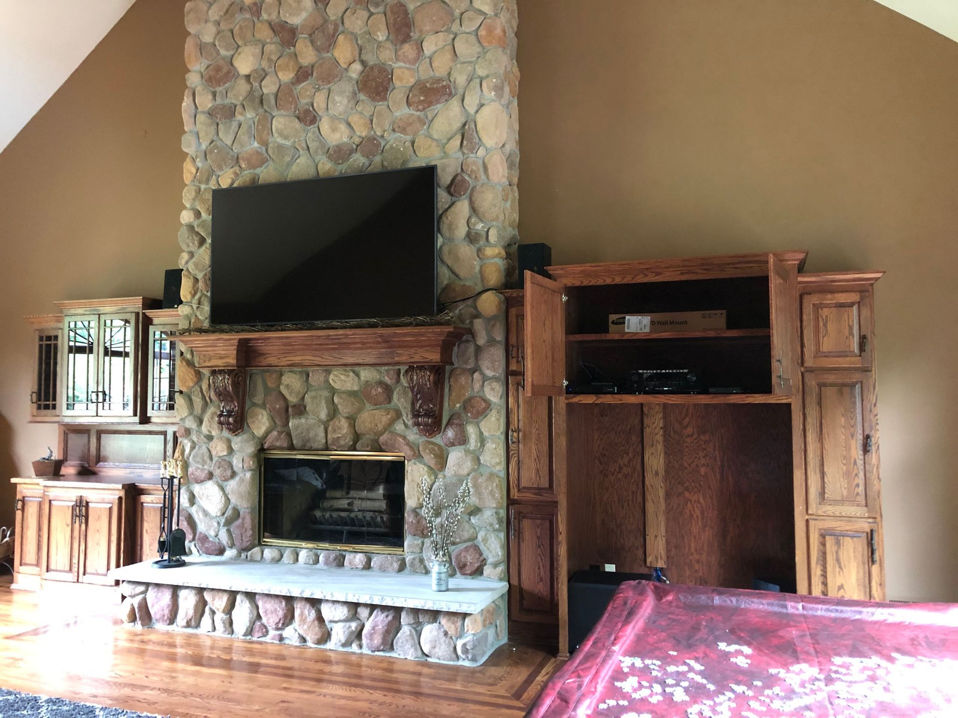 Living room with stone fireplace, TV, wooden cabinets, and red rug by Audio Video Concepts