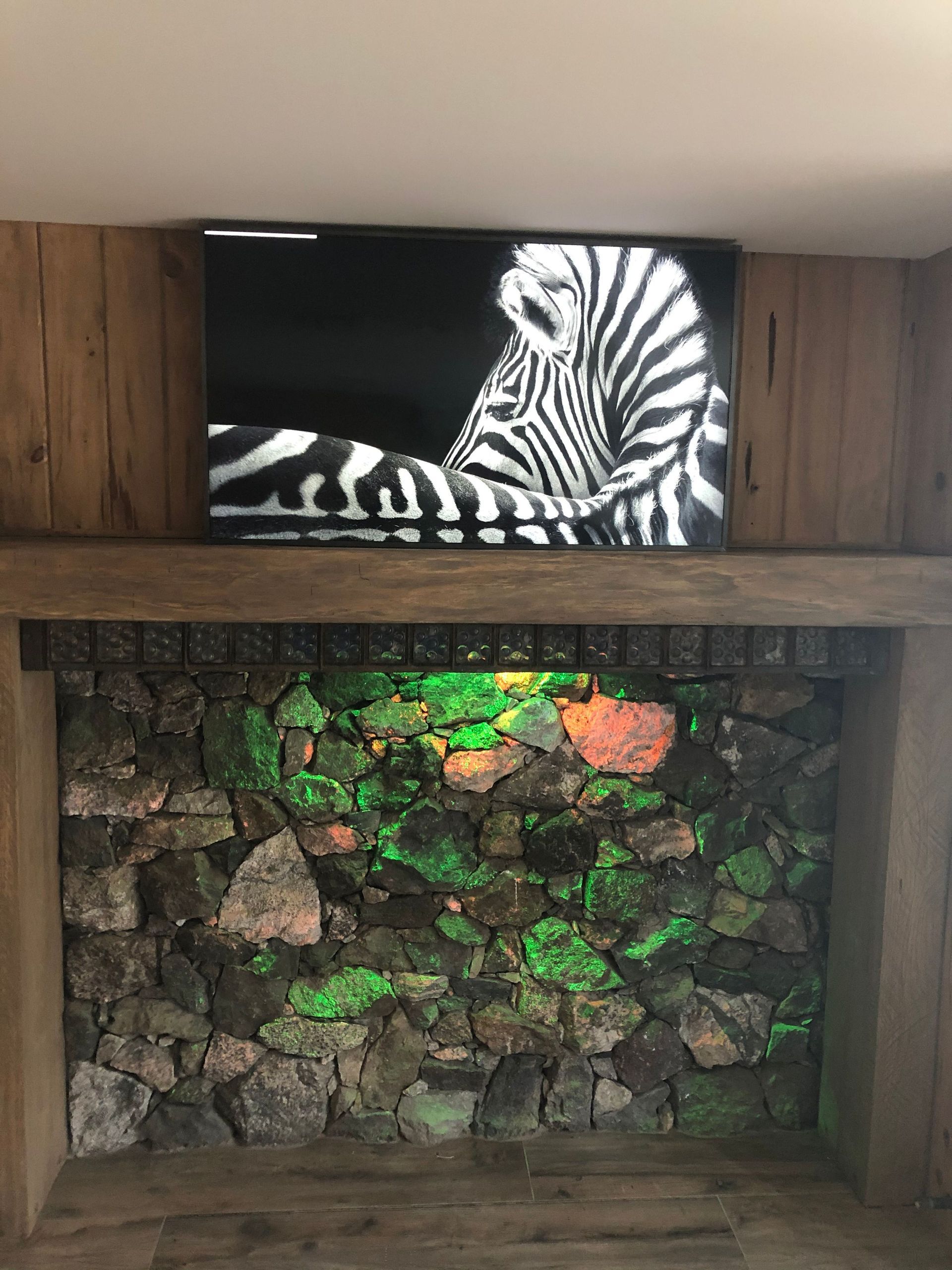 Zebra artwork above a stone fireplace with glowing green and orange lights by Audio Video Concepts