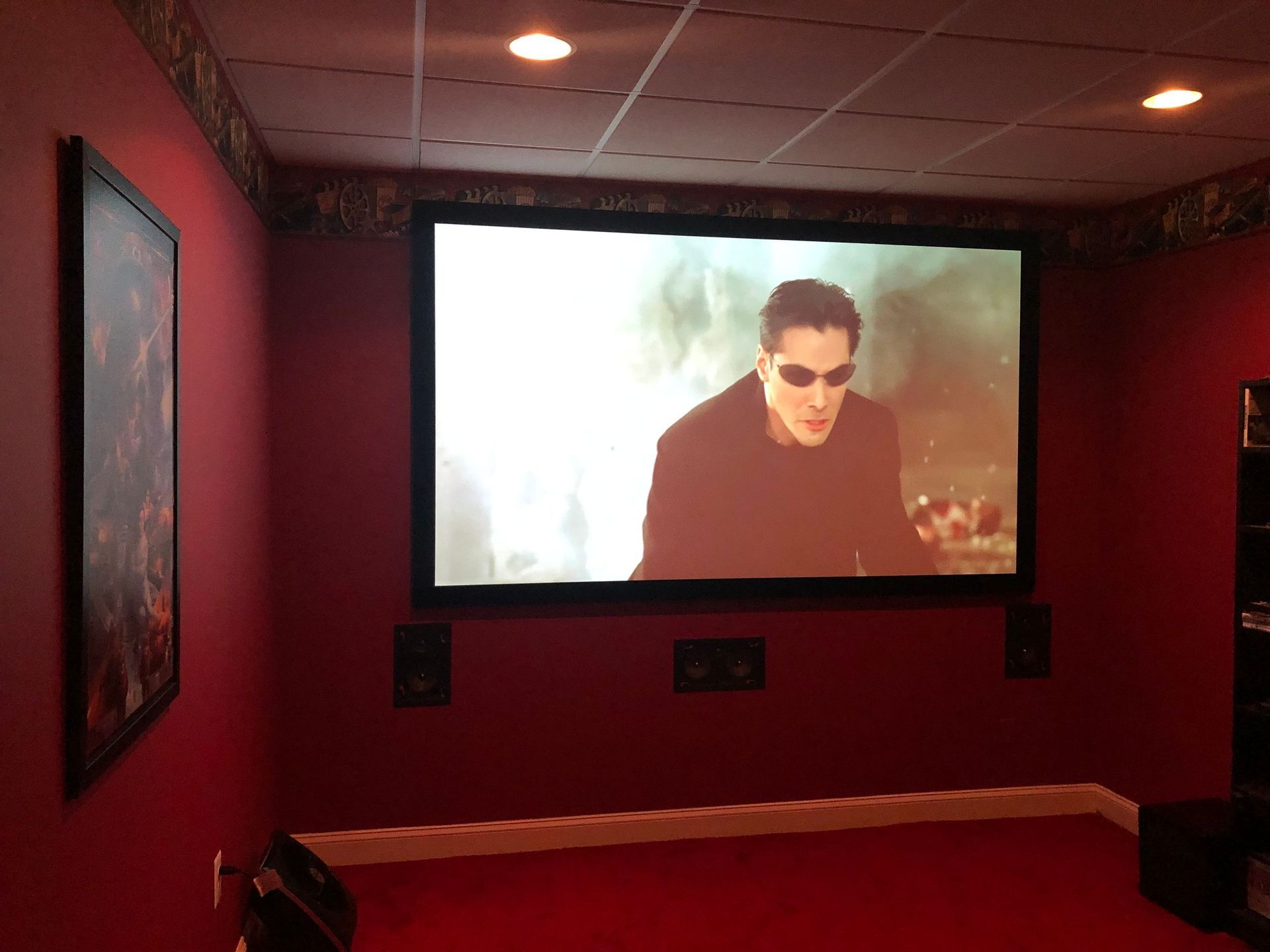 Home theater room with red walls and a movie playing on a large screen by Audio Video Concepts