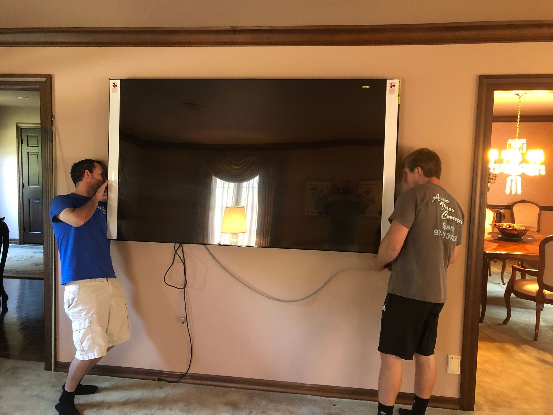Two men carrying a large flat-screen TV through a doorway in a living room by Audio Video Concepts