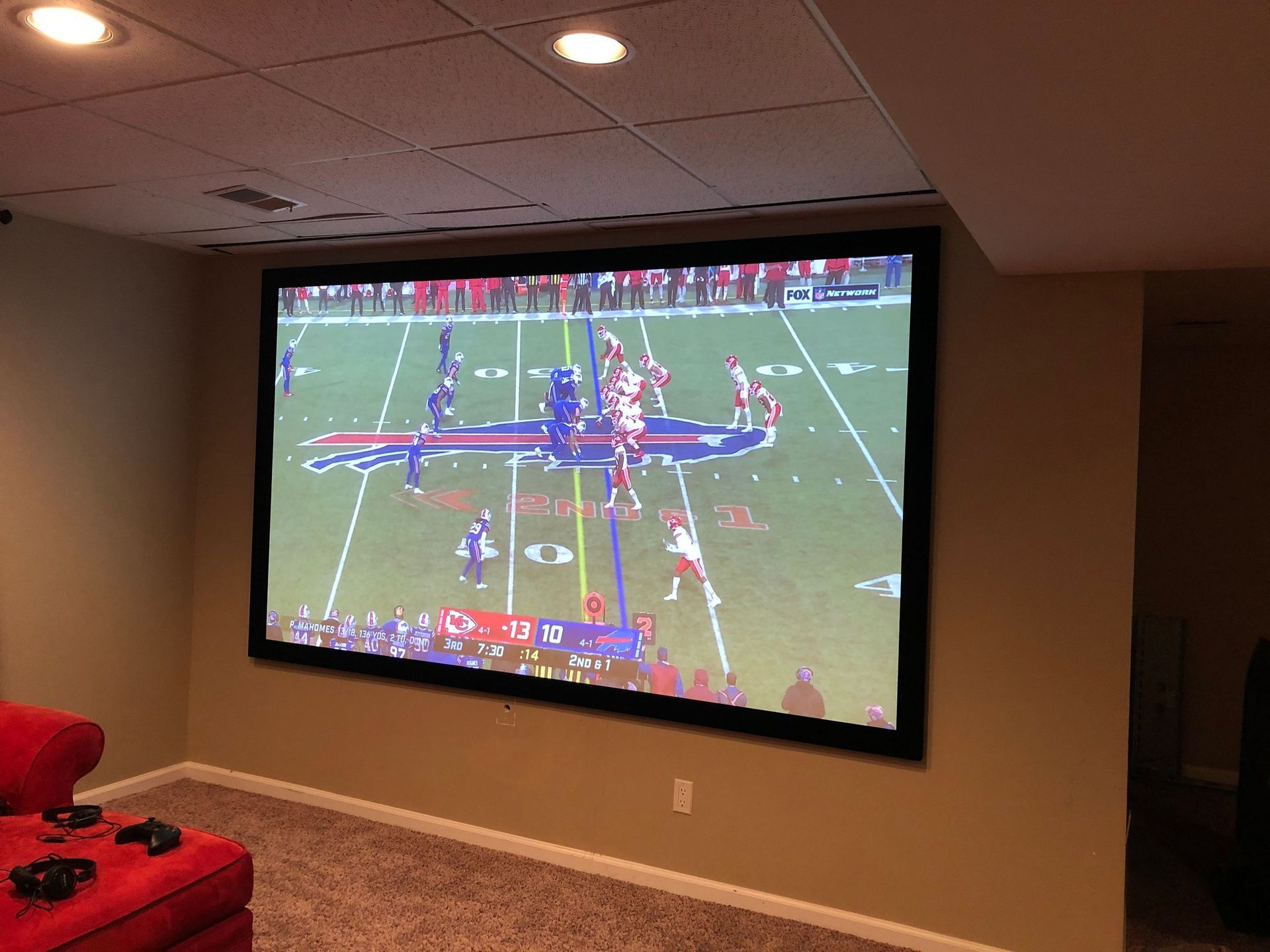 Projected football game on a living room wall, with red chairs and ceiling lights visible by Audio Video Concepts