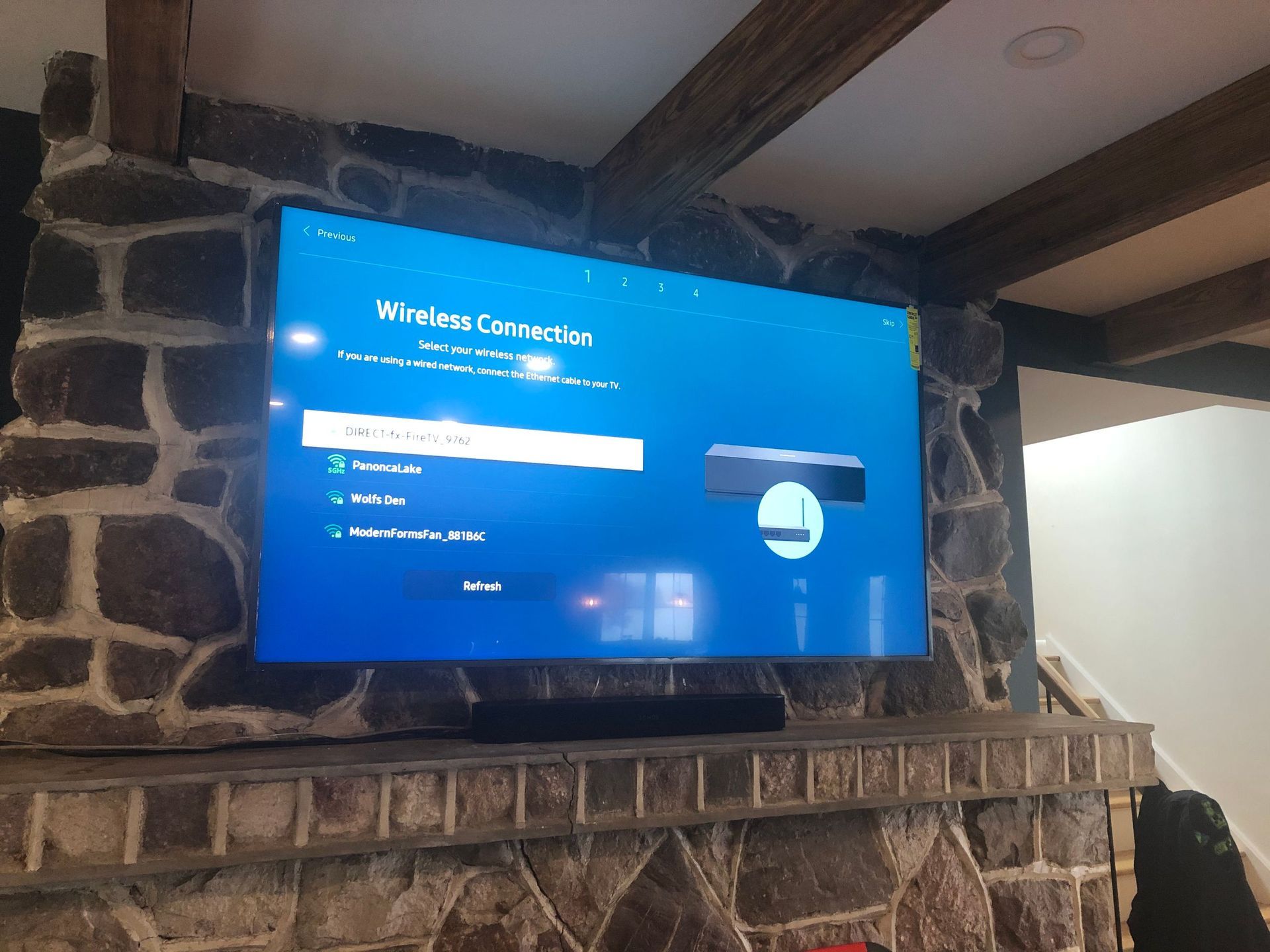 Wall-mounted TV displaying a blue Xbox sign-in screen above a stone fireplace in a rustic room by Audio Video Concepts