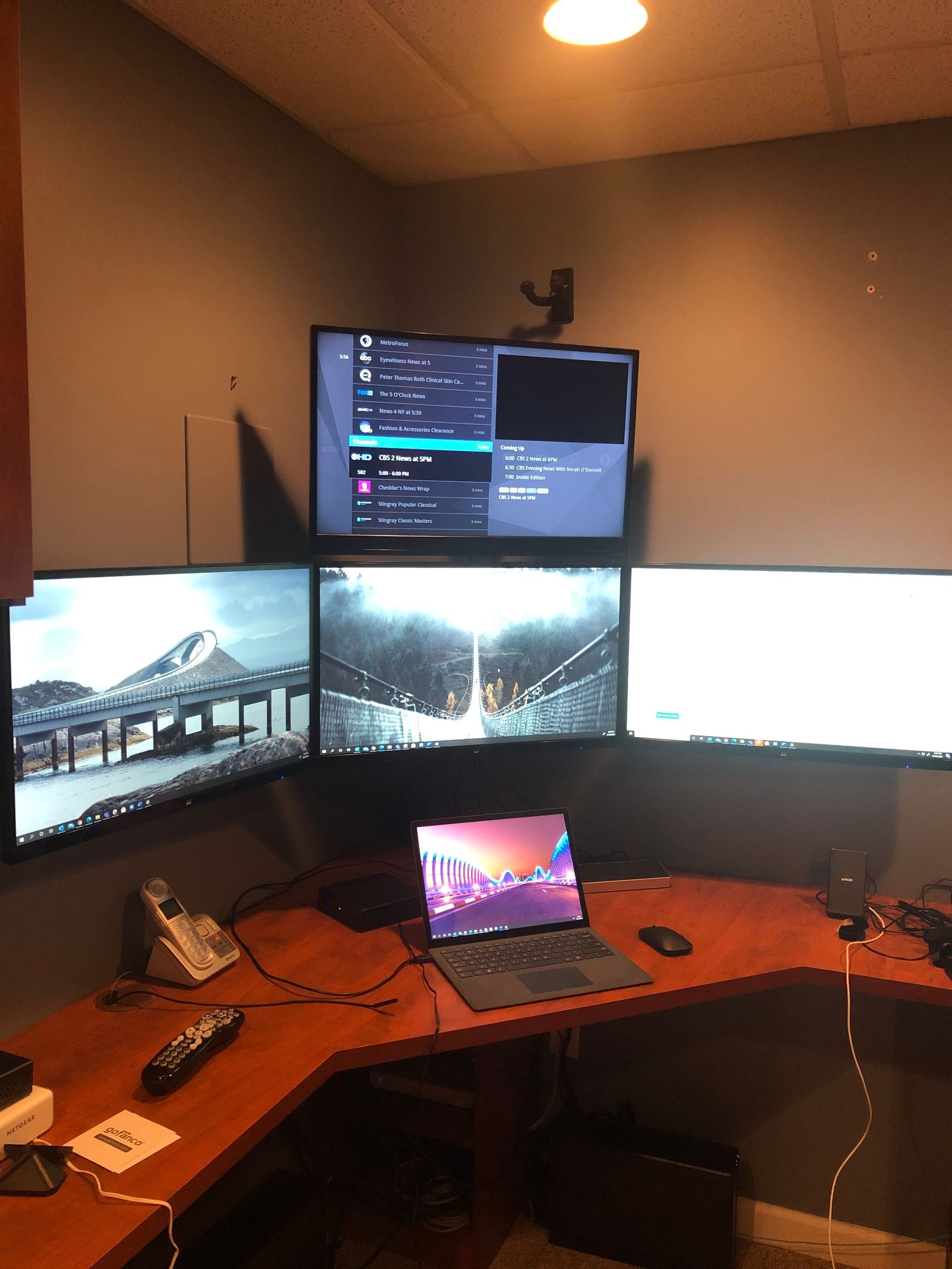 Curved desk with multiple monitors and a laptop in a dimly lit home office setup by Audio Video Concepts