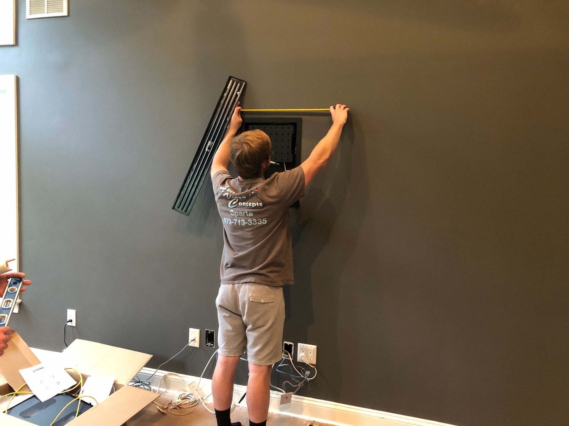 Person mounting a black wall shelf in a room with tools and boxes on the floor by  Audio Video Concept