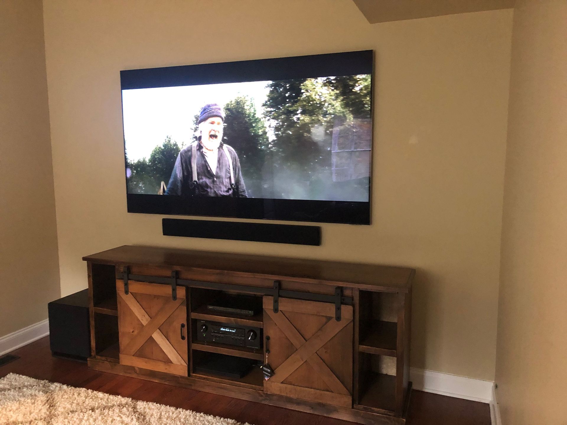Living room TV playing a scene above a wooden media console on a beige wall by Audio Video Concepts