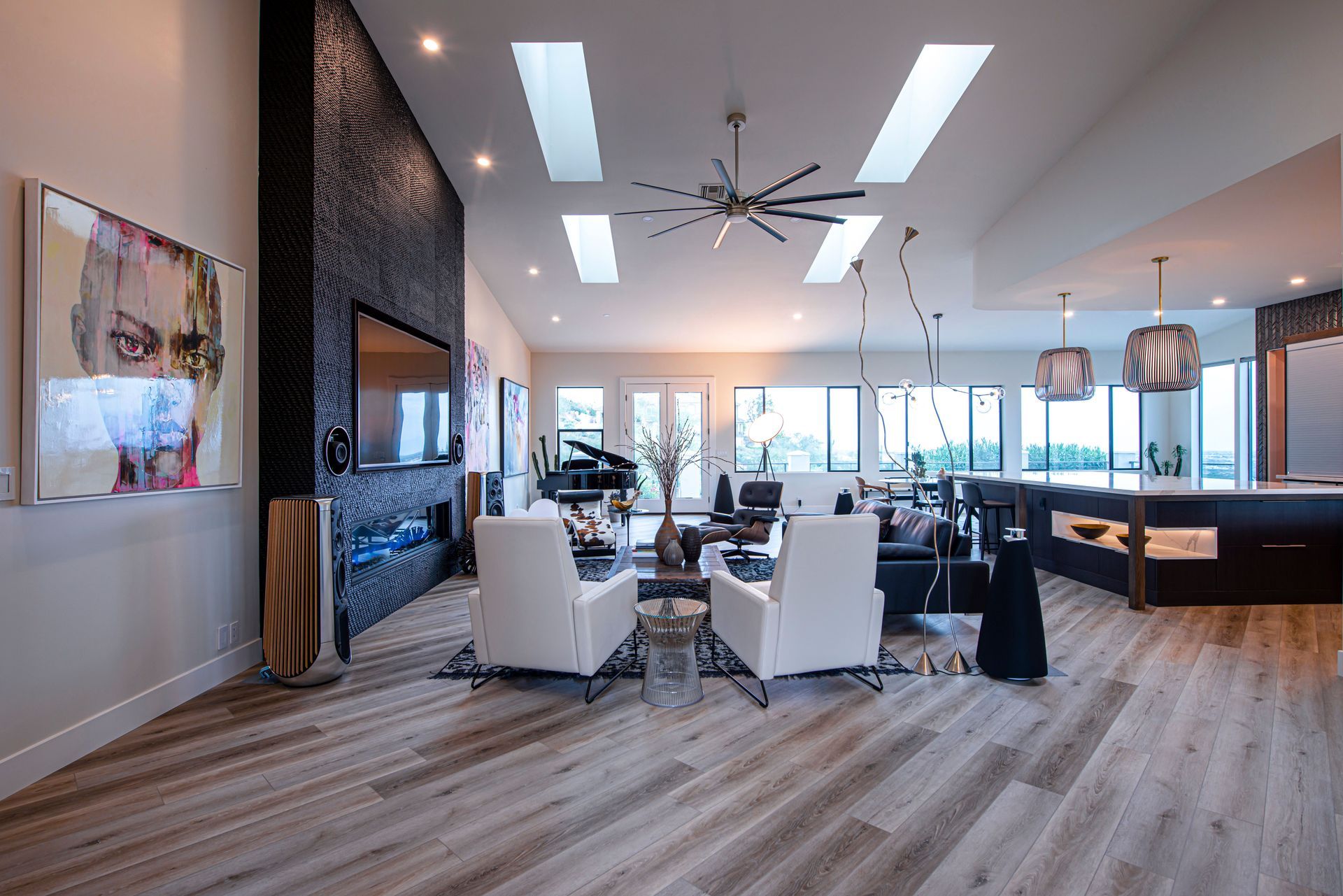 Modern living room with white chairs, dark fireplace, wood floor, and large windows overlooking a view by Audio Video Concept