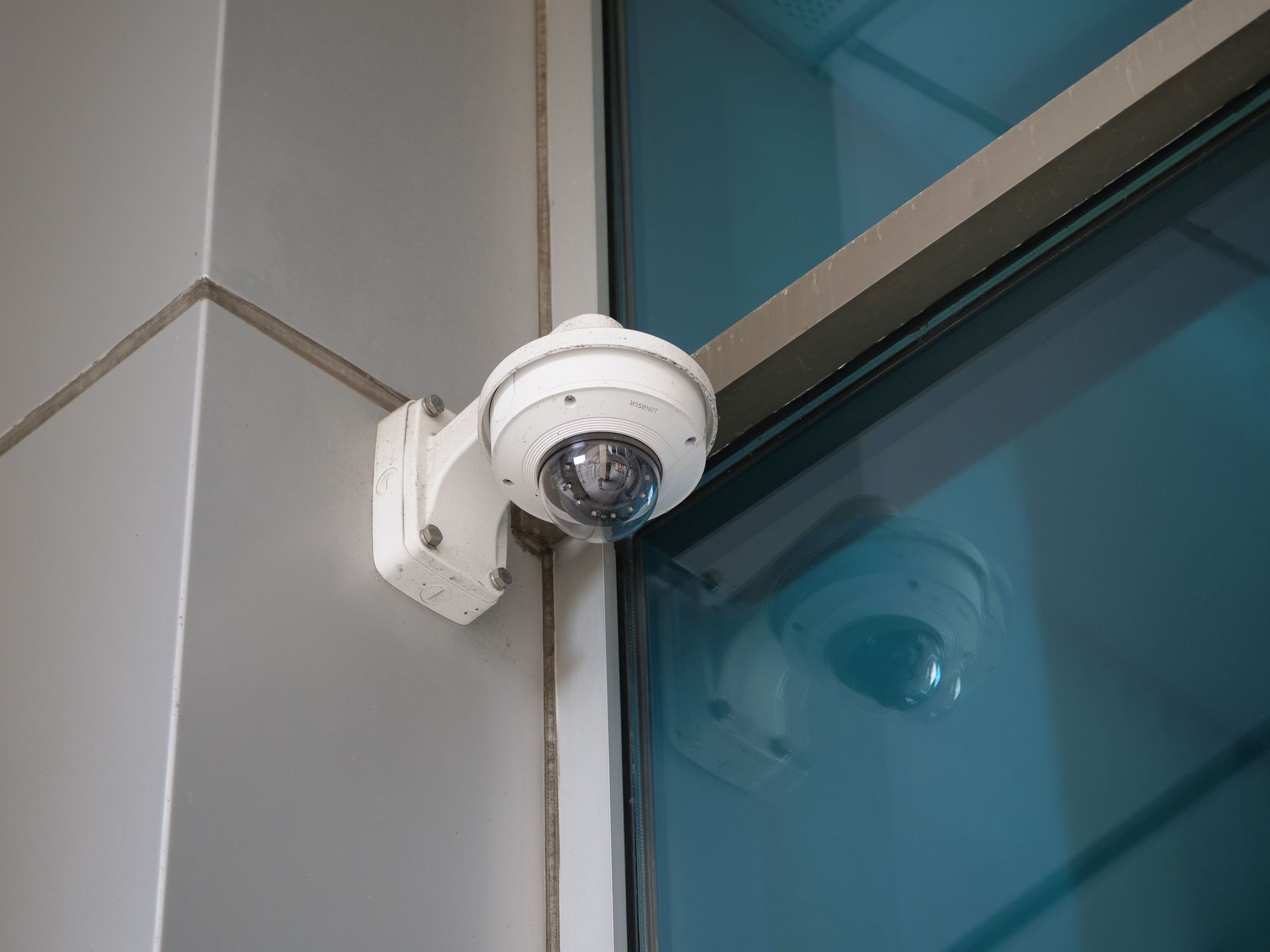 Security camera mounted on a wall beside a blue glass window by Audio Video Concept