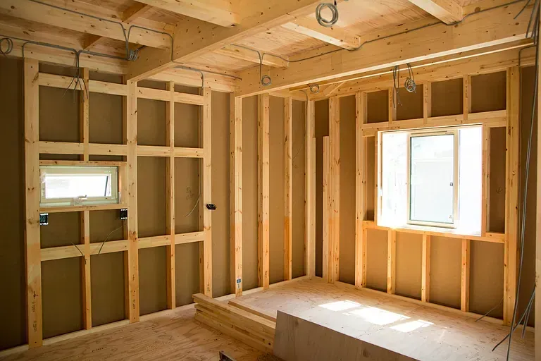 Unfinished room framed with exposed wood studs, two windows, and a built-in bench or platform by Audio Video Concept