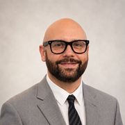 Portrait of a smiling man in glasses and a gray suit against a plain light background