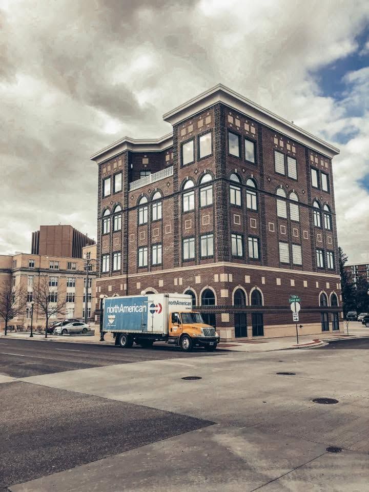 Brick multi-story building on a city street with a white delivery truck parked in front under cloudy skies