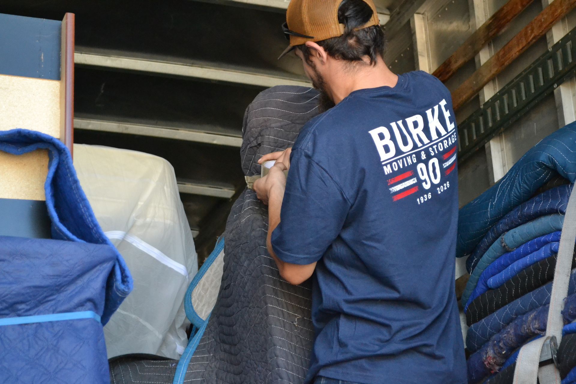 Two workers loading a large rolled mat into a truck among stacked blue mats.