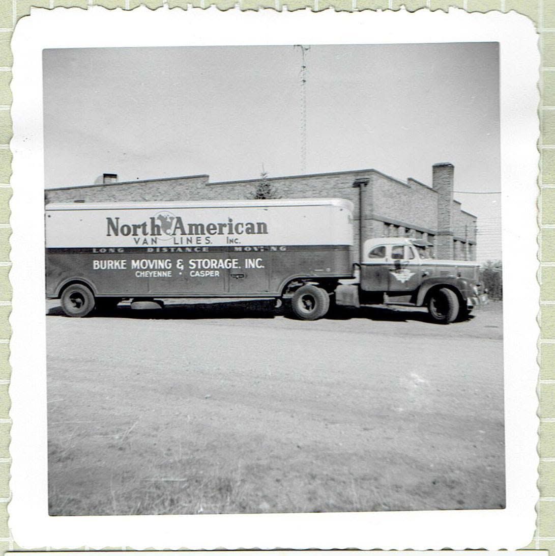 Black-and-white photo of a North American moving truck parked beside a brick building.