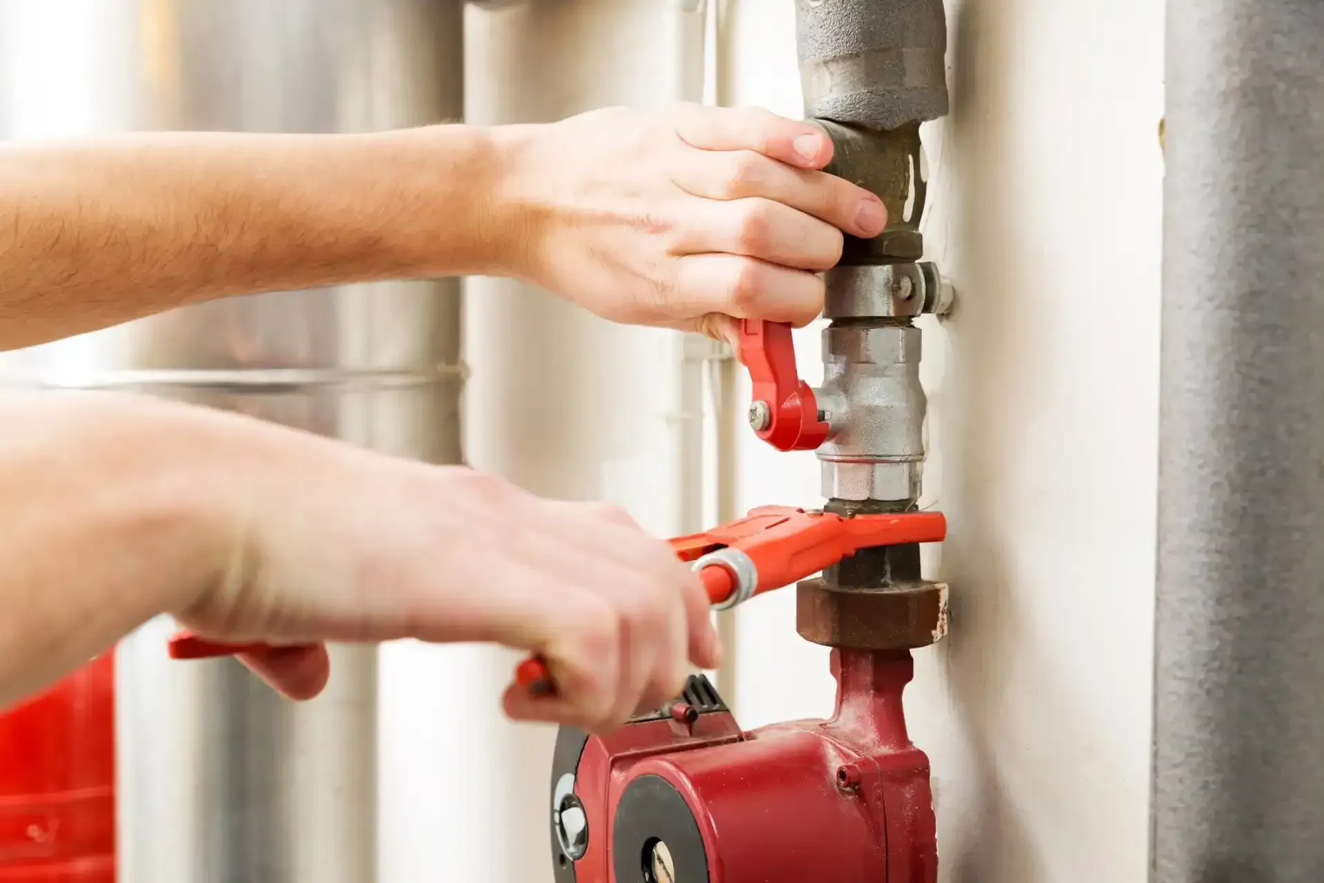 Hand tightening a pipe fitting under a sink with adjustable wrenches