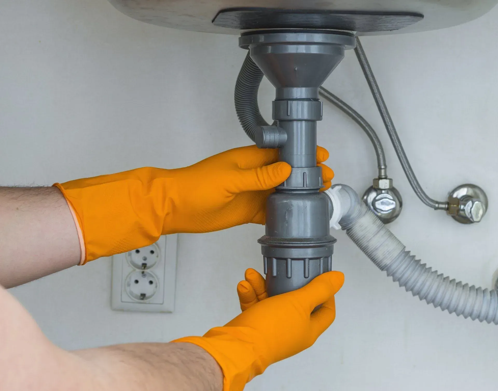 Gloved hands tightening a gray sink drain pipe under a bathroom sink