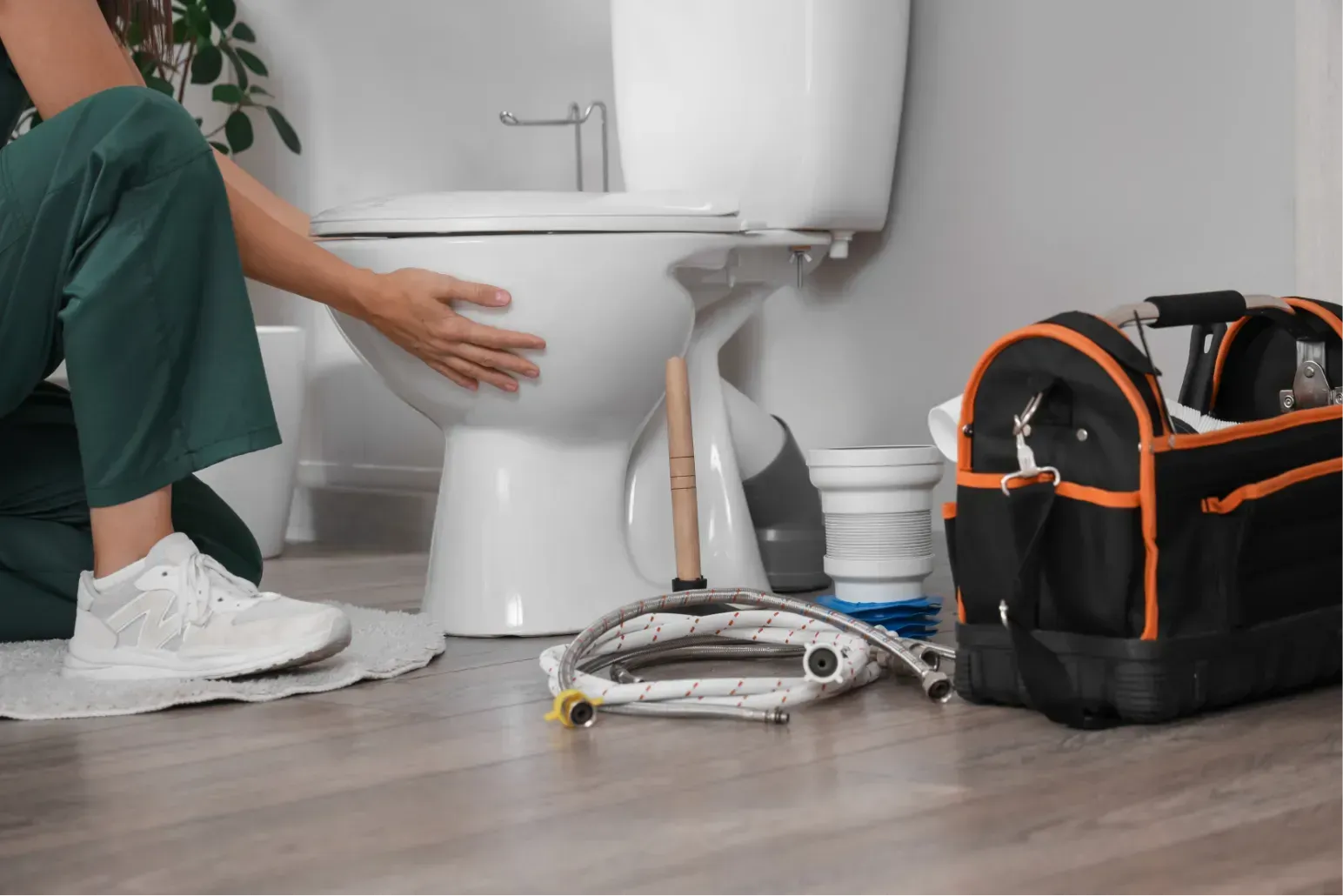 Plumber working on a bathroom toilet with tools and a repair bag on the floor