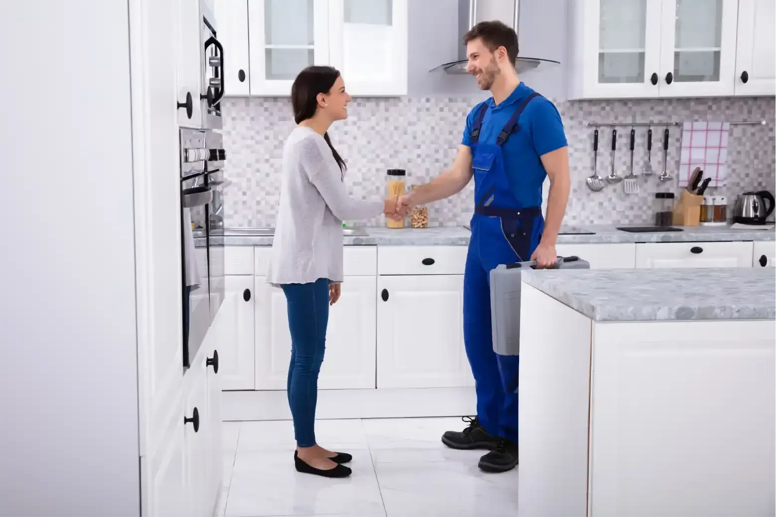 Two coworkers in a bright kitchen exchanging a drink, with white cabinets and marble countertops.