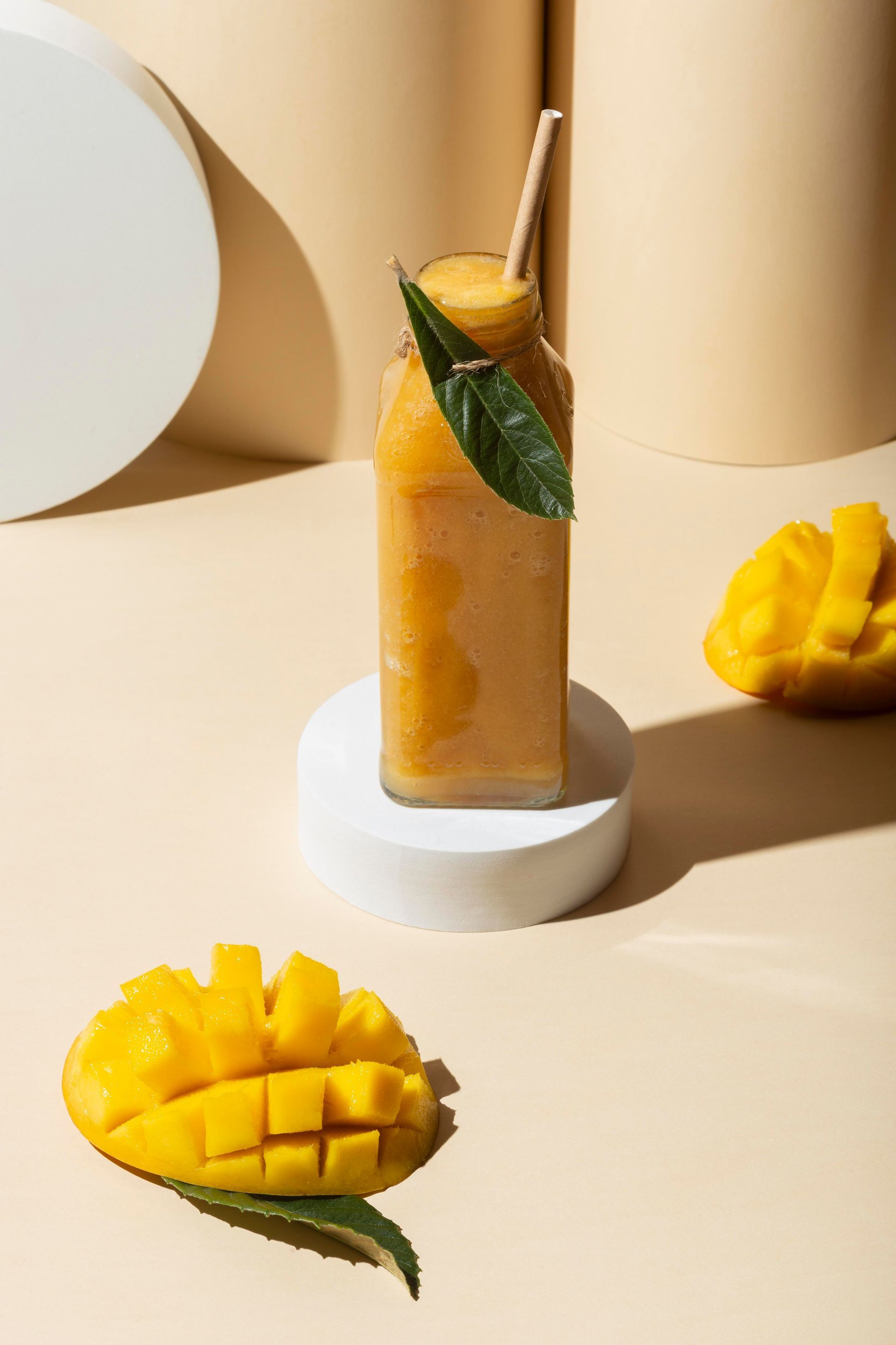 Een fles mangosap met een rietje en mangoschijfjes op een tafel.