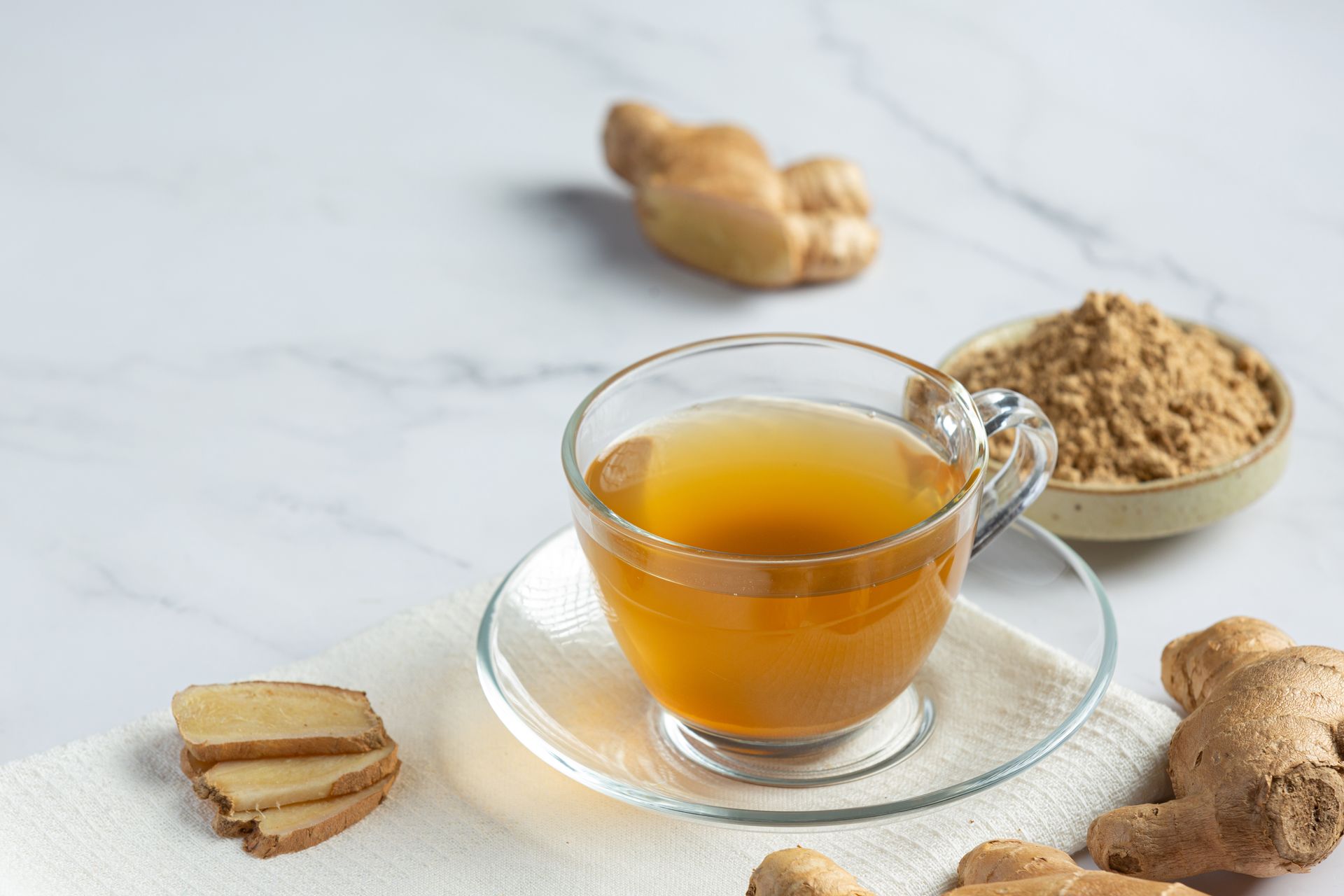 Een kopje gemberthee Yofelix gemberdrank staat op een schoteltje naast gember.
