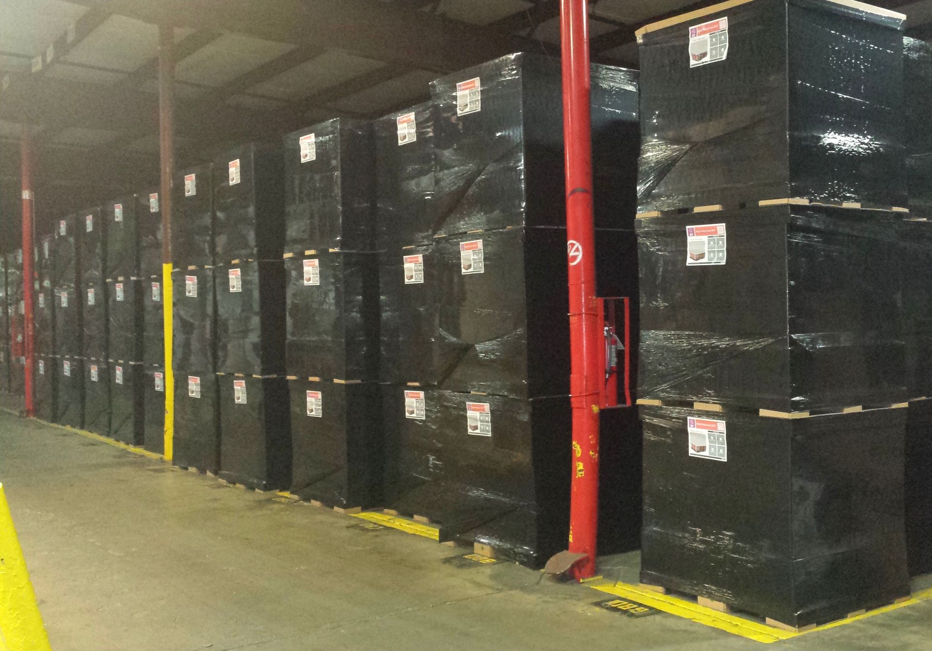 Rows of black stretch-wrapped retail shipments stacked on lightweight corrugated pallets in a distribution warehouse.