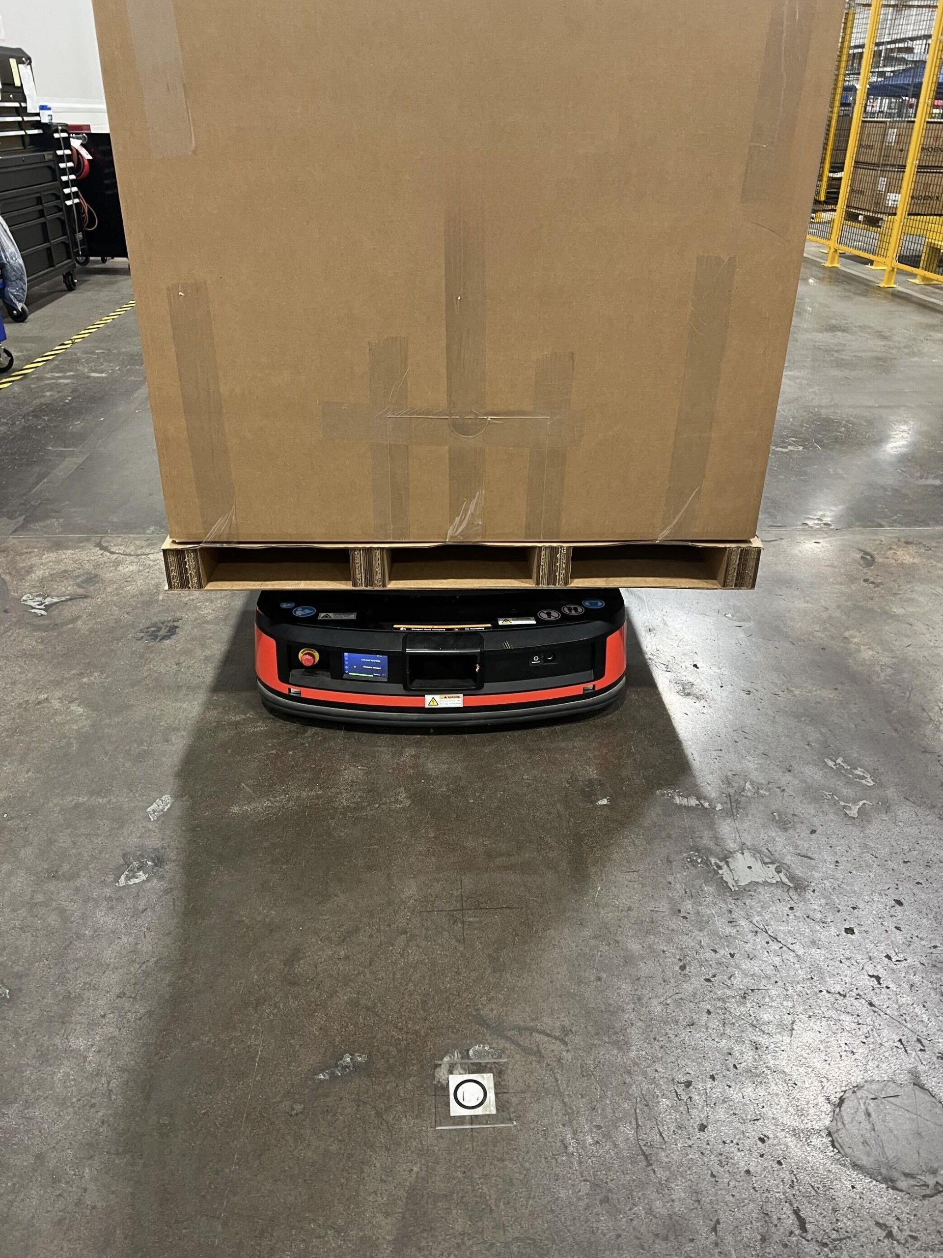 Corrugated pallet supporting a large pallet on an agv during material-handling in a manufacturing facility.