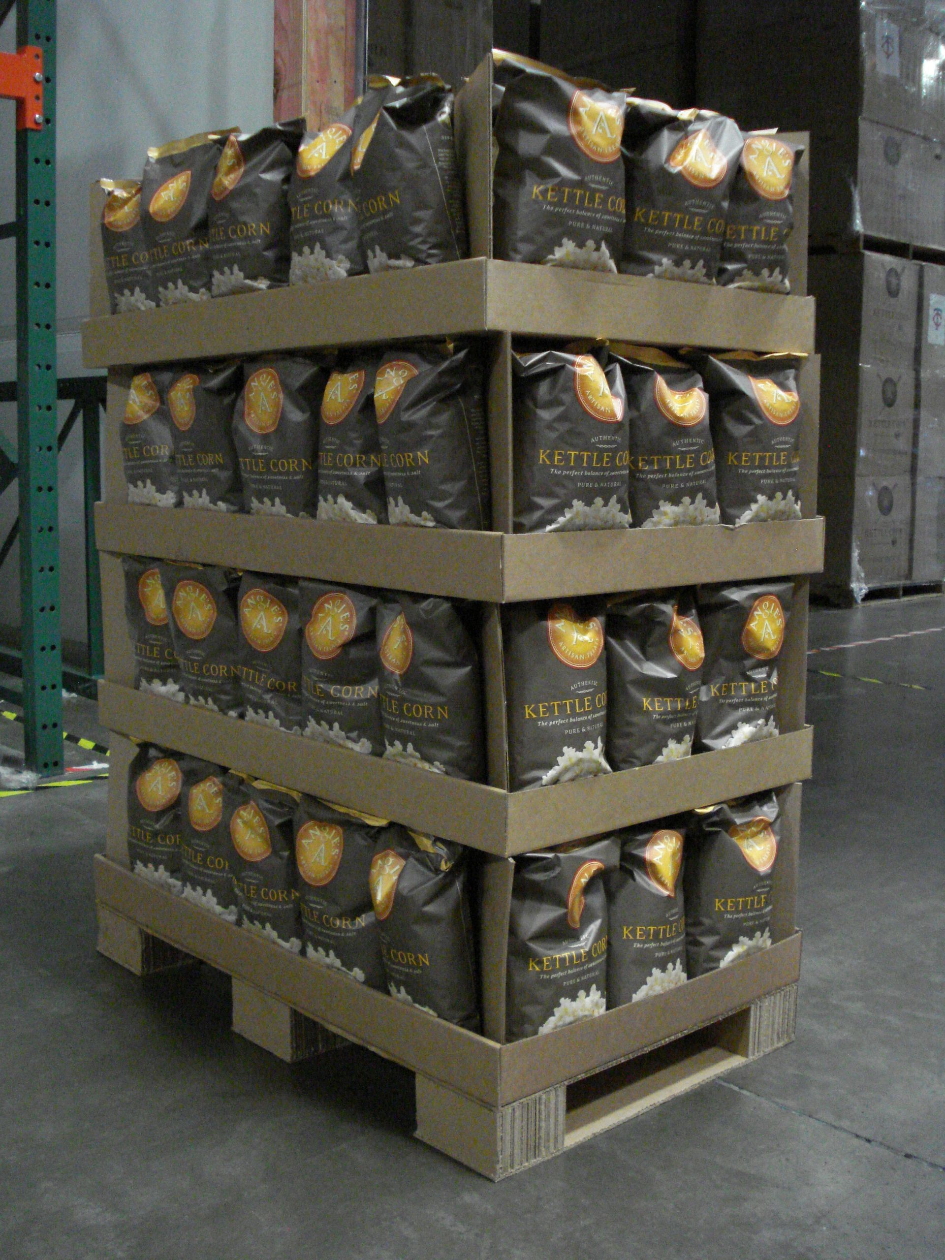 Angled view of a corrugated retail display loaded with bagged snacks, showing the half-pallet construction and blocks.