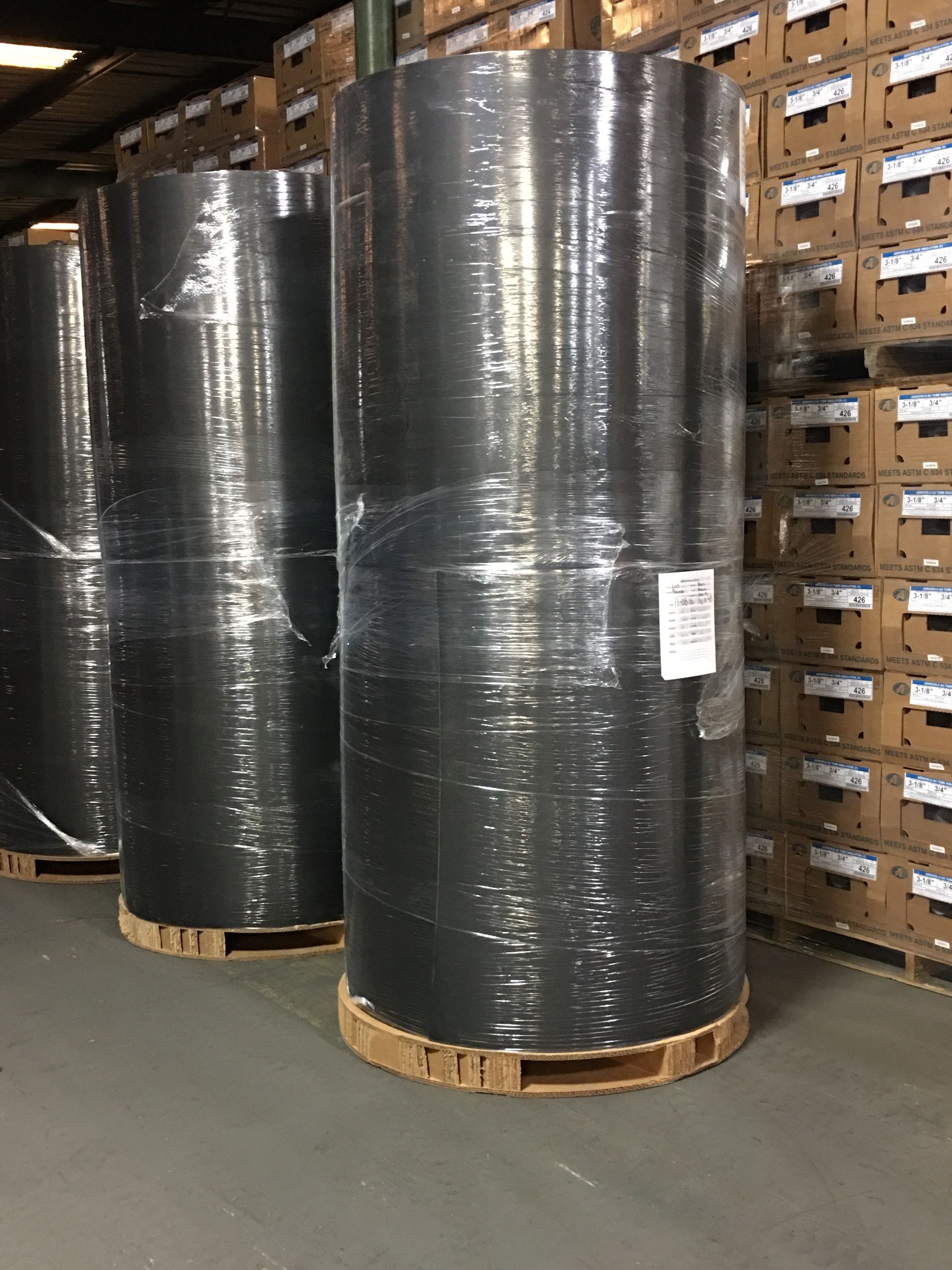 Large industrial rolls wrapped in protective film on round corrugated pallets inside a warehouse.