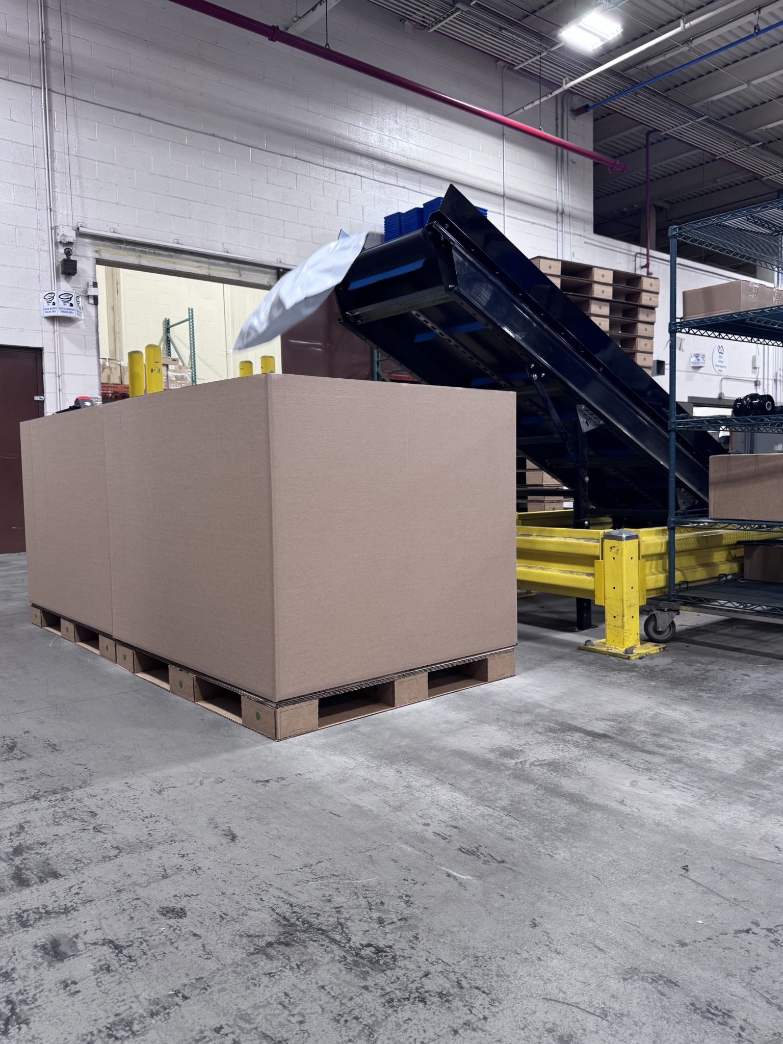 Large corrugated bulk container on an Ecodek pallet beside packaging equipment in a healthcare supply distribution facility.