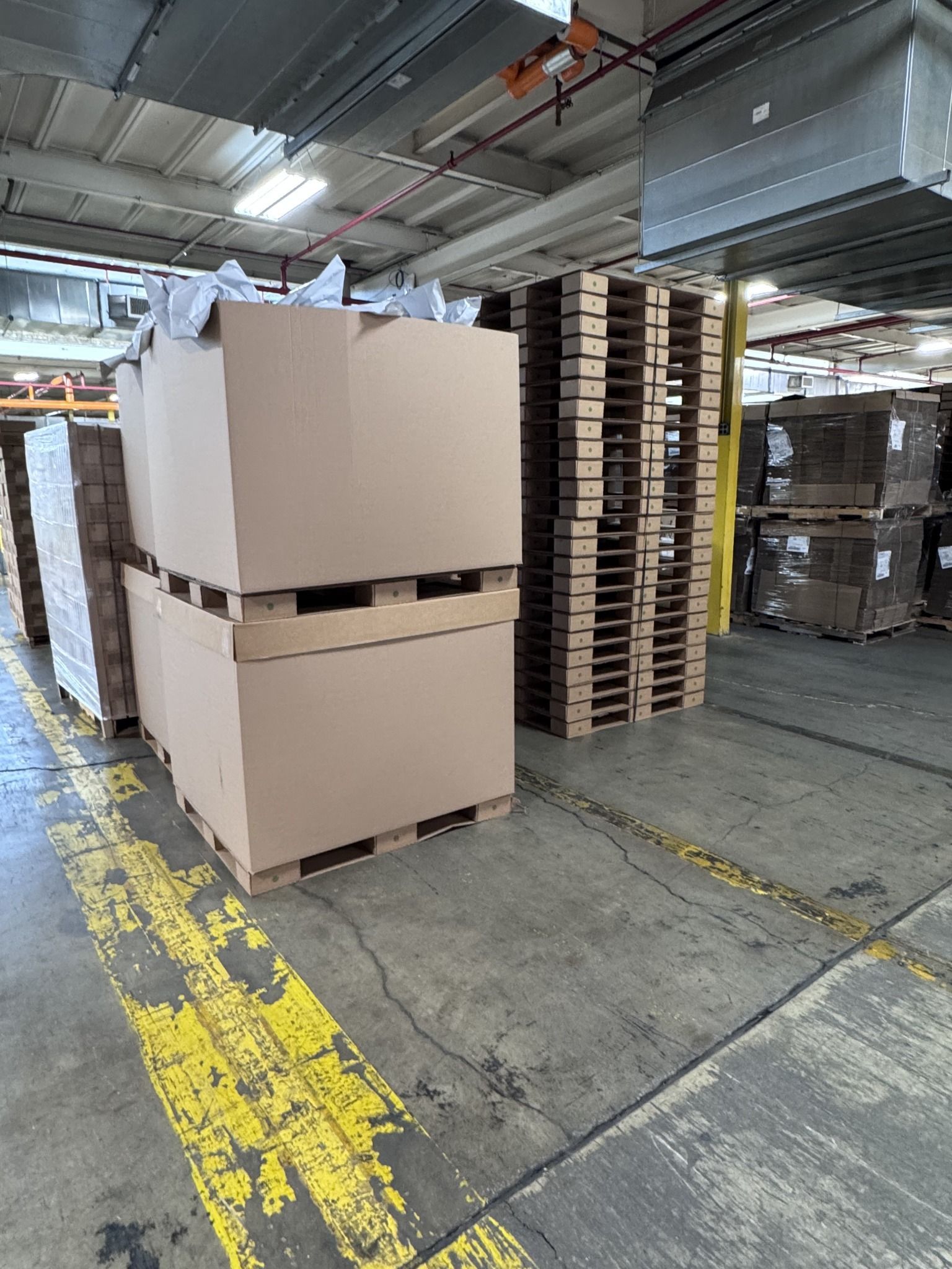 Warehouse employee working beside an open bulk container on a corrugated pallet, with powered material-handling equipment.