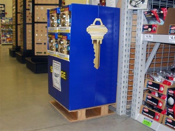 Compact quarter-size corrugated pallet with inset runners supporting a freestanding retail key display inside a store.