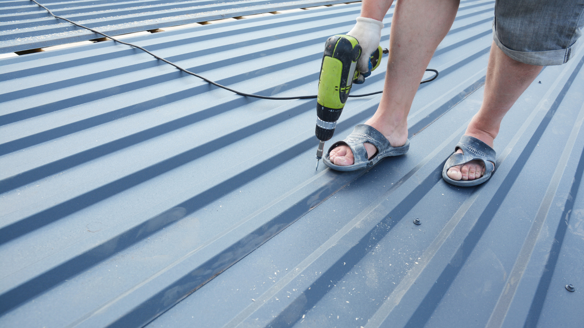 Person using a power drill on a metal roof panel with a cable nearby