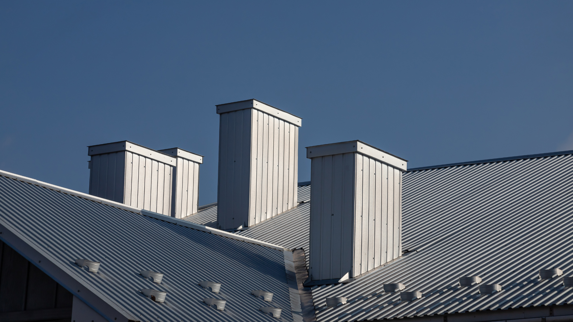 Corrugated metal rooftop with three white chimneys against a clear blue sky