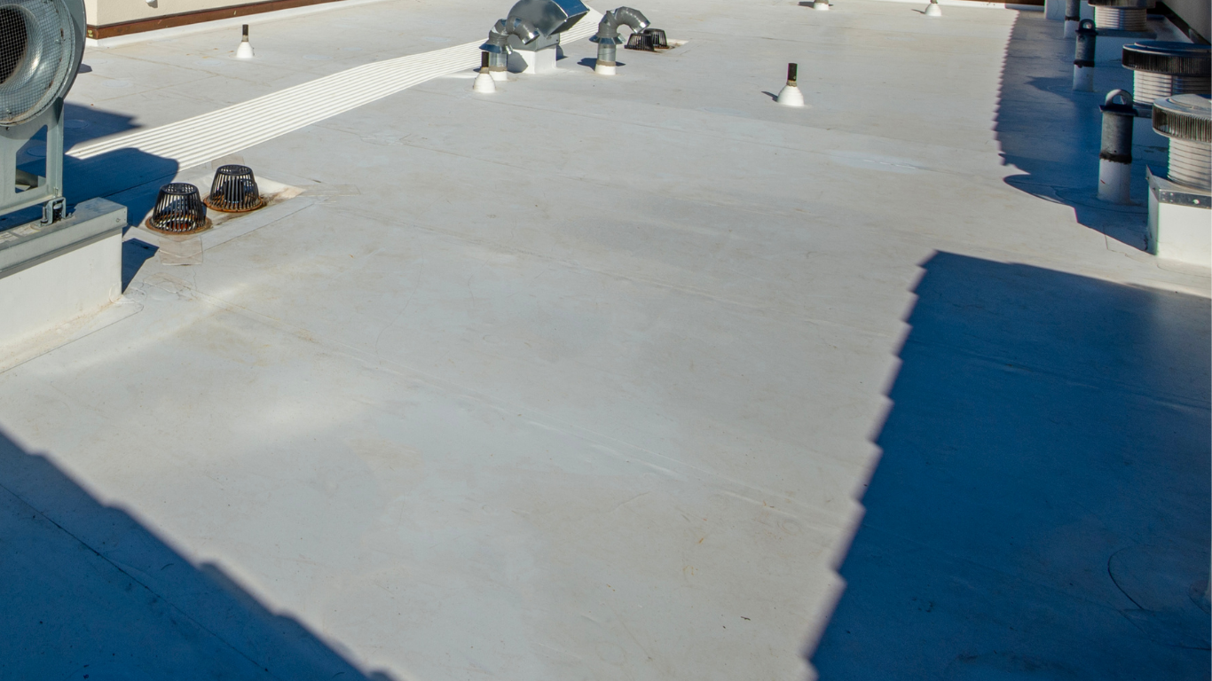 Worker on a shingled roof near trees, installing or repairing roofing under a clear blue sky
