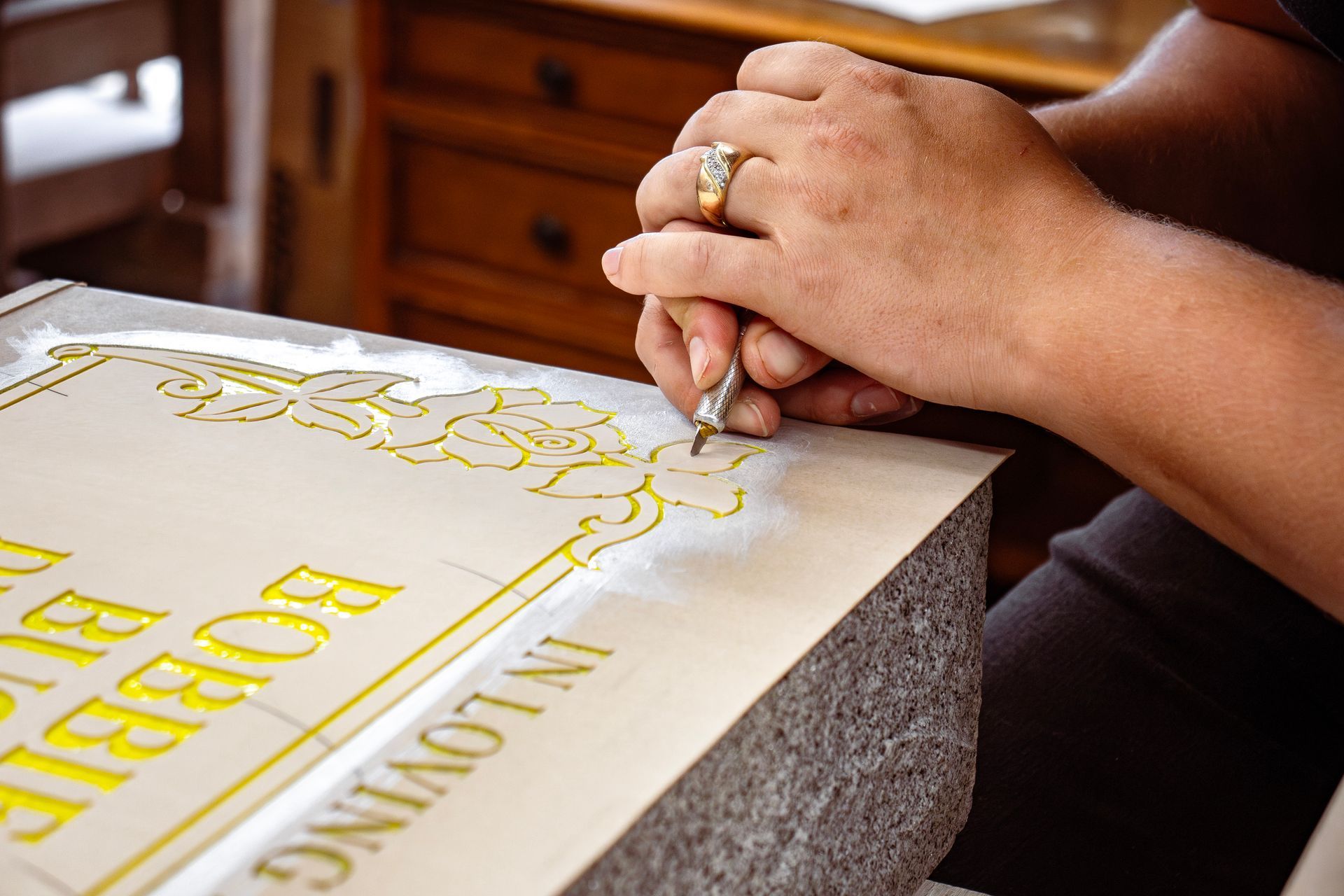 A person carves gold lettering and floral designs into a stone.
