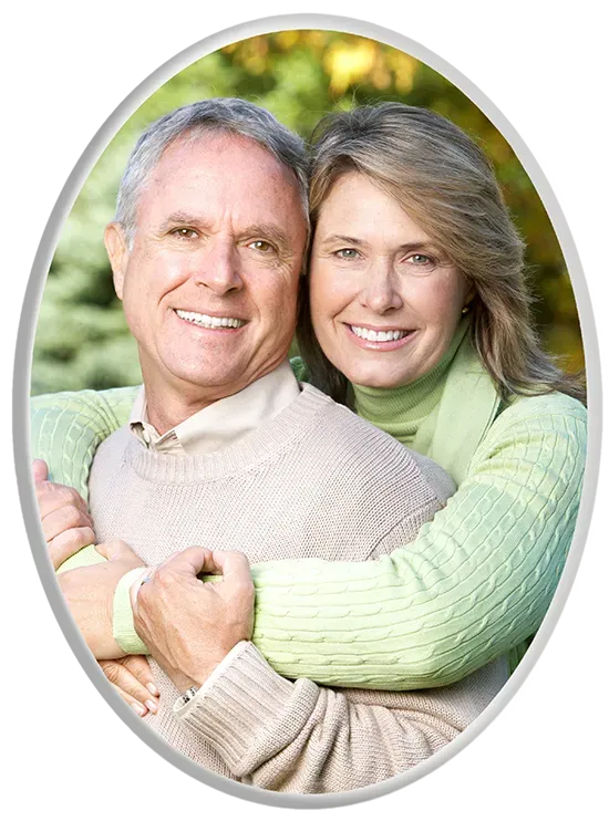 Couple smiling, embracing outdoors. Woman's arms around man, green and beige clothing, oval frame.