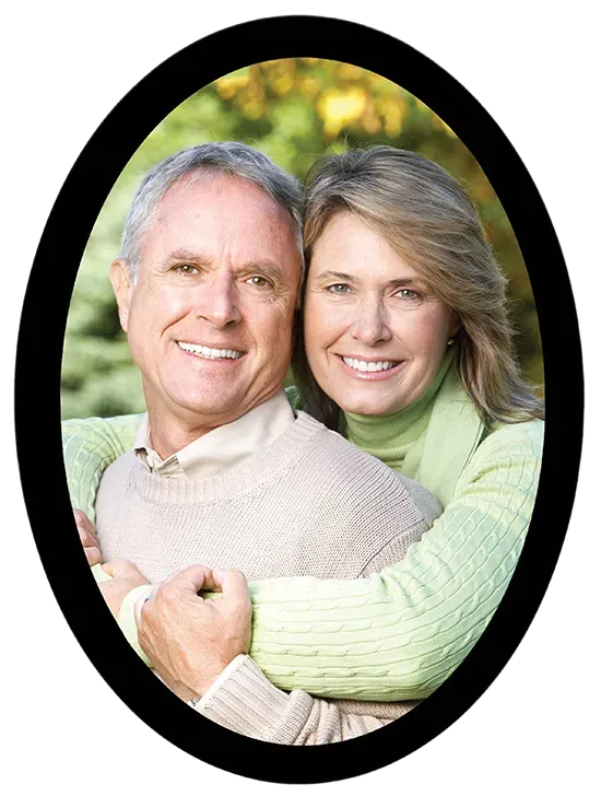 Smiling couple embracing, framed in a black oval. Outdoors with green foliage background.