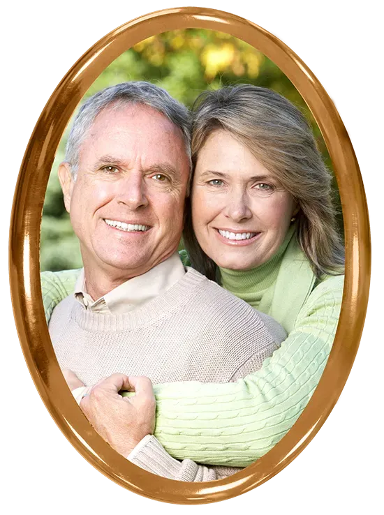 Smiling couple embracing in an oval gold frame; man in sweater, woman in green.