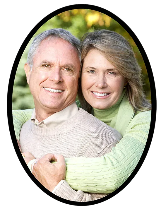 Couple embracing, smiling; outdoor setting. Man in light sweater; woman in green sweater.