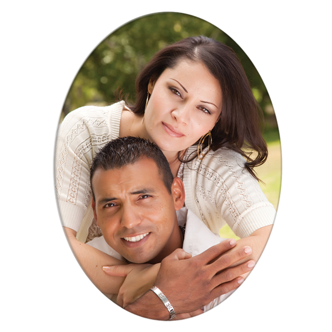 Couple embracing, woman behind man. Both smiling in a blurred outdoor setting.