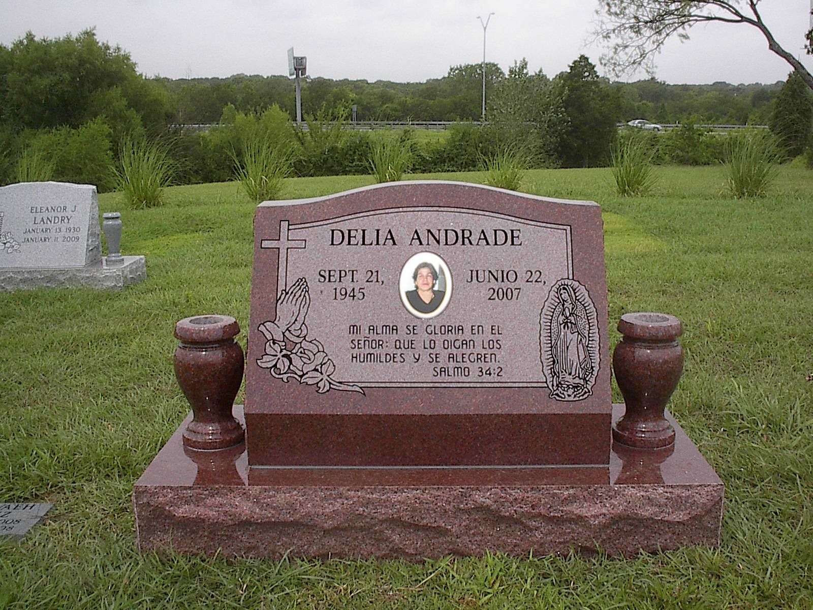 Grave of Delia Andrade with photo, text, and decorative elements on a red granite headstone in a cemetery.