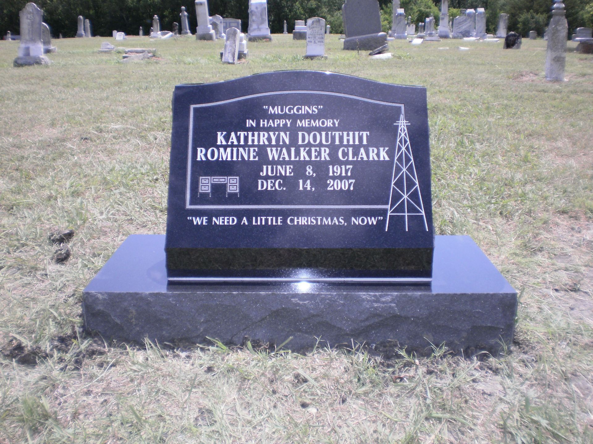 Black headstone with inscriptions and an oil derrick sketch in a grassy cemetery.