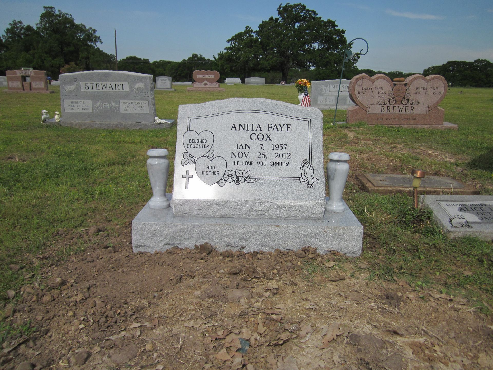 Gravestone in a grassy cemetery; the headstone is gray with engraved text.