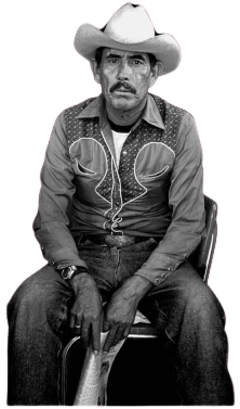 Man in cowboy hat and shirt sits in a chair, looking forward, hands in lap. Black and white.